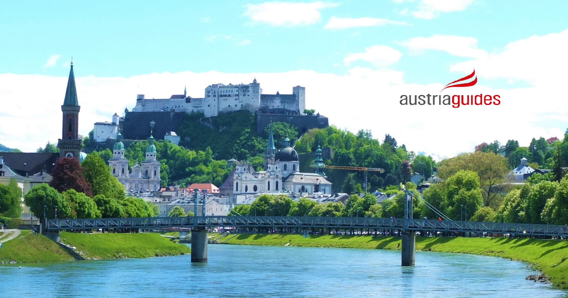 Das Bild zeigt die Altstadt mit der Festung Hohensalzburg auf dem Festungsberg. Viele Kirchen sind zu sehen: Dom, Universitätskirche, Franziskanerkirche und andere. Der Fluß Salzach und eine Brücke sind auch zu sehen.