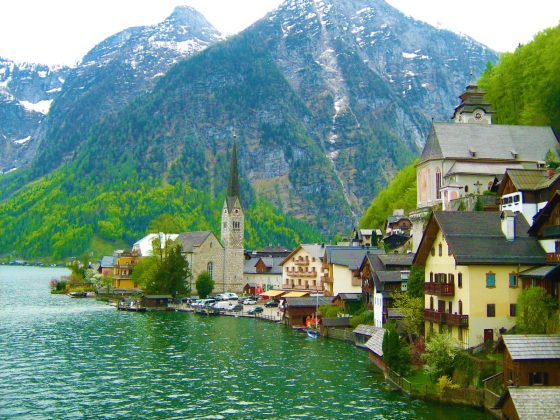 A little romantical austrian village with a name Hallstatt with a church with a long church tower on a green looking lake, on tha background are bluish high mountains.